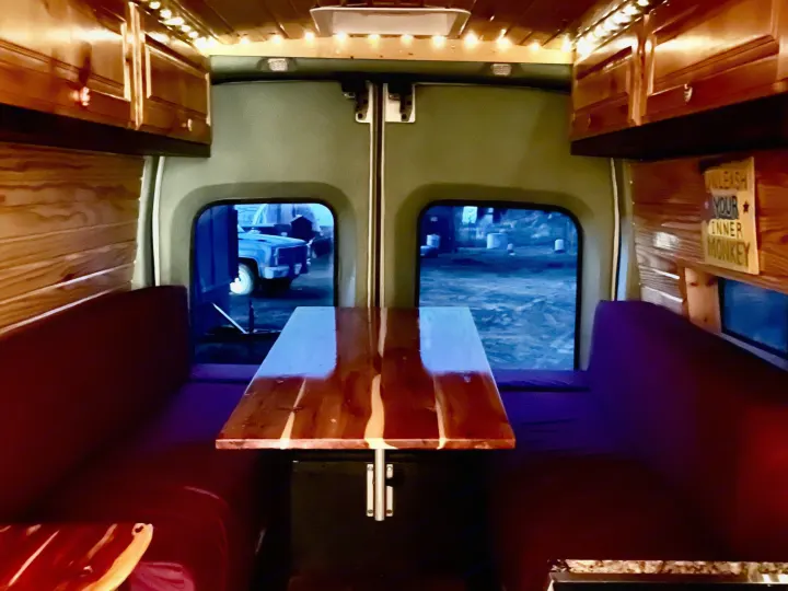 Cozy RV rental interior with a wooden dinette, bright LED lights, and rich wood paneling, ready for adventure.. Ford Transit 350 High Roof EXT 2020