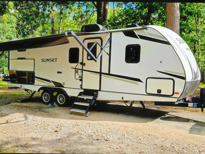 RV rental: A white Sunset Trail travel trailer with an extended awning, parked on a gravel campsite among trees.. Crossroads RV Sunset Trail Super Lite 2022