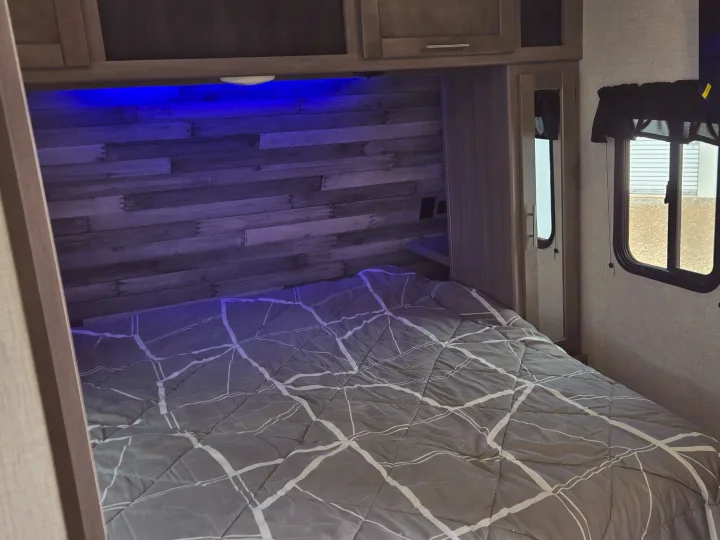 This cozy RV rental bedroom features a patterned comforter, blue accent lighting, a mirror, and a thermostat for comfortable travel.. Crossroads RV Sunset Trail Super Lite 2022