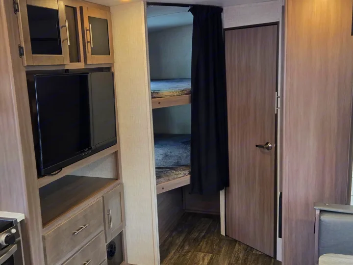 RV rental interior: kitchen, TV, bunk beds with curtain, and dining nook. Compact and functional living space.. Crossroads RV Sunset Trail Super Lite 2022