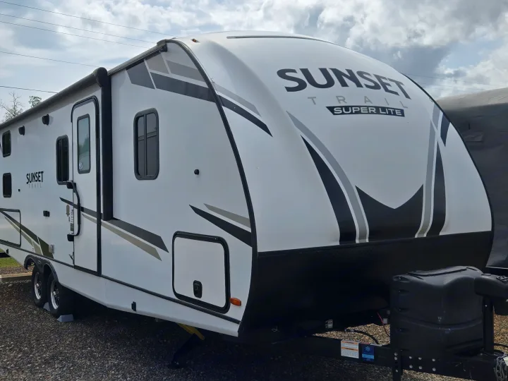 White Sunset Trail Super Lite travel trailer for rv rental, showcasing its side profile, awning, and front hitch area.. Crossroads RV Sunset Trail Super Lite 2022