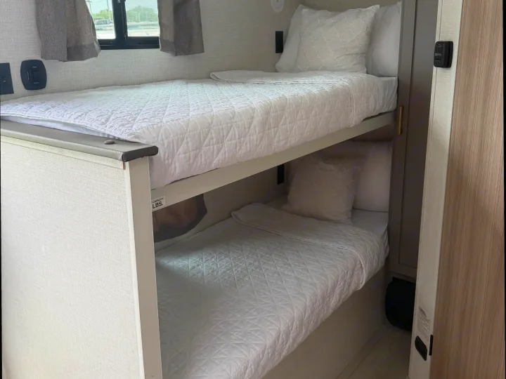 Inside an RV rental: two neatly made bunk beds with white quilted bedding, offering comfortable travel accommodation.. KZ Sportsmen Classic 130BH 2026