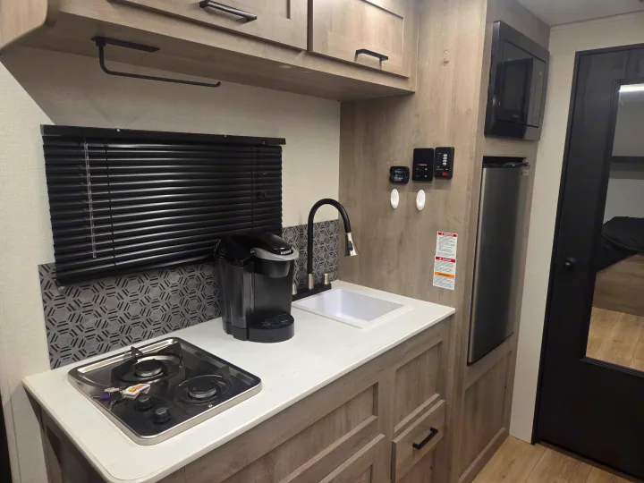 Compact rv rental kitchen: features a sink, stove, Keurig, microwave, fridge, and stylish wooden cabinets & backsplash.. Cruiser RV Embrace 2025