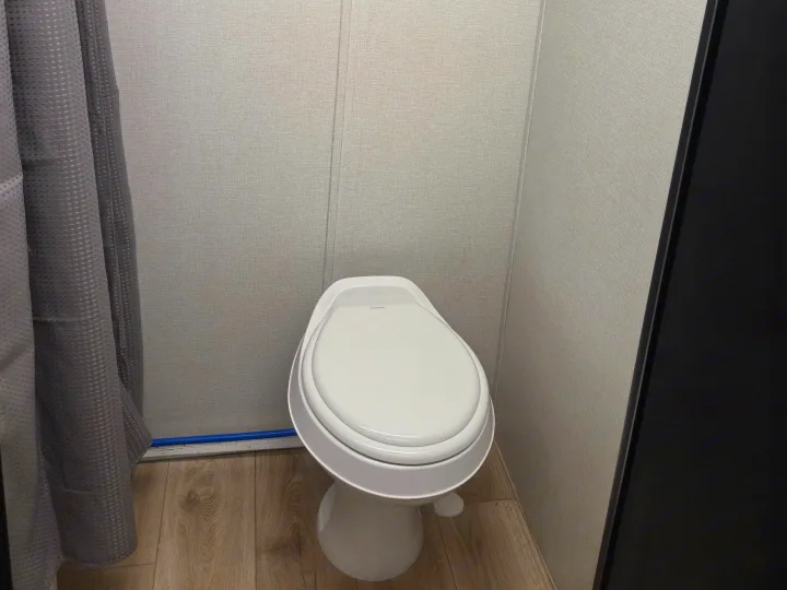 Compact RV rental bathroom with a white Dometic toilet, grey paneled walls, wood-look floor, and a shower curtain.. Cruiser RV Embrace 2025