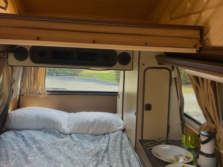 Inside this spacious RV rental: a comfy bed, dining counter with plates, and rear window view. Ideal for travel adventures.. Volkswagen Westfalia 1986