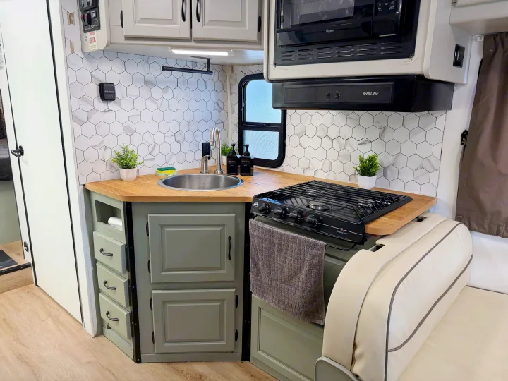 Inside an RV rental: a modern kitchen with light wood counters, gray cabinets, hexagonal tile backsplash, sink, and stovetop.. Thor Majestic 2015