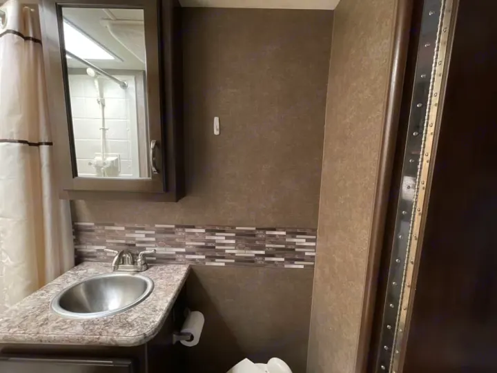 Inside an RV rental bathroom: compact sink, mirrored cabinet, shower, toilet, and stylish backsplash. Essential amenities on the go.. Thor Freedom Elite 2020