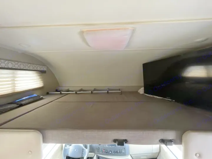 Overhead bunk bed in this cozy RV rental, with a comfy mattress, TV, and window. Ideal sleeping space for your motorhome journey.. Thor Freedom Elite 2020