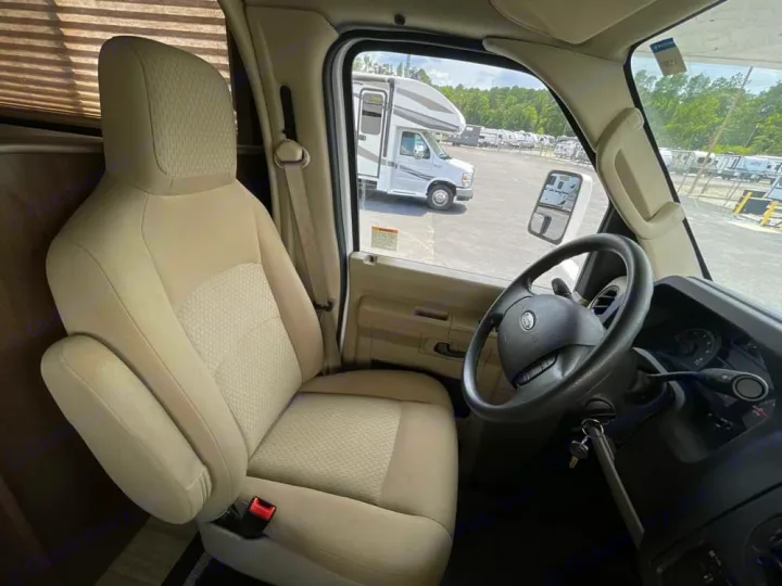 Inside an RV rental, the driver's cockpit features a tan seat, steering wheel, and views of a motorhome lot outside.. Thor Freedom Elite 2020