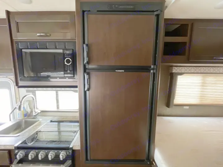 RV rental kitchen and sleeping area: Dometic fridge, microwave, stove, sink, and part of a bed with mattress.. Thor Freedom Elite 2020