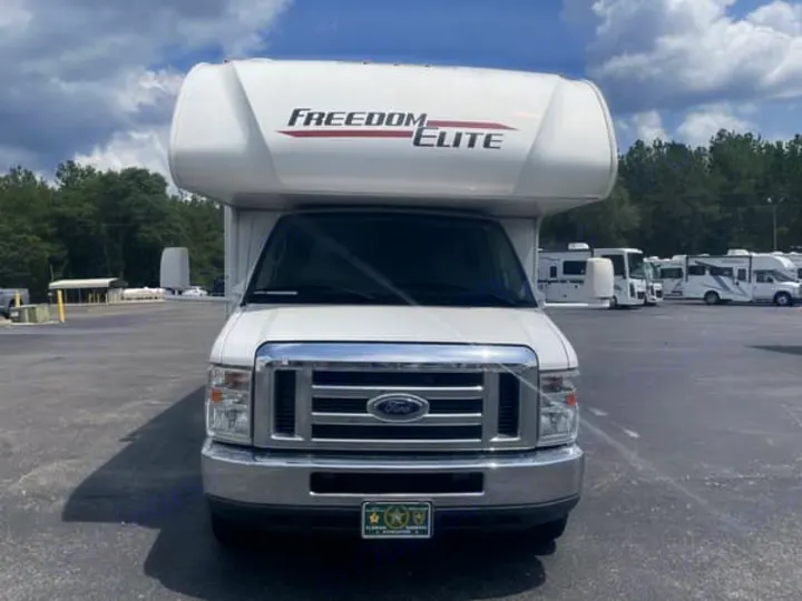 Front view of a white Freedom Elite Class C RV for rv rental, parked in a lot with other RVs under a partly cloudy sky.. Thor Freedom Elite 2020