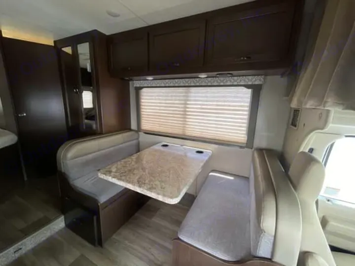 Experience this RV rental's cozy interior, featuring a comfortable dinette with cushioned benches, a table, and overhead cabinets.. Thor Freedom Elite 2020