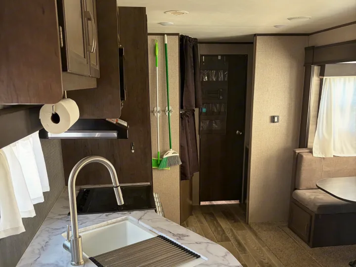 RV rental interior: kitchen with sink and paper towels, dinette, and clever storage including broom, mop, and door organizer.. Jayco Jay Flight SLX Rocky Mountain Edition 2021