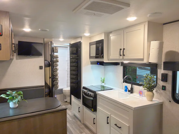 This bright RV rental interior features a modern kitchen, dining area, and compact bathroom with bunk beds, ideal for travel.. Jayco Jay Flight SLX 2024