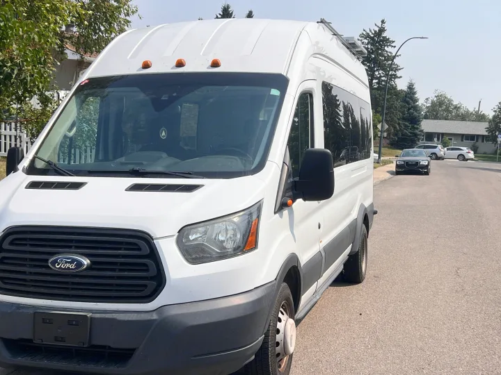 White high-roof Ford Transit van, a potential RV rental or camper conversion, parked on a residential street with solar panels.. Ford Transit 2016