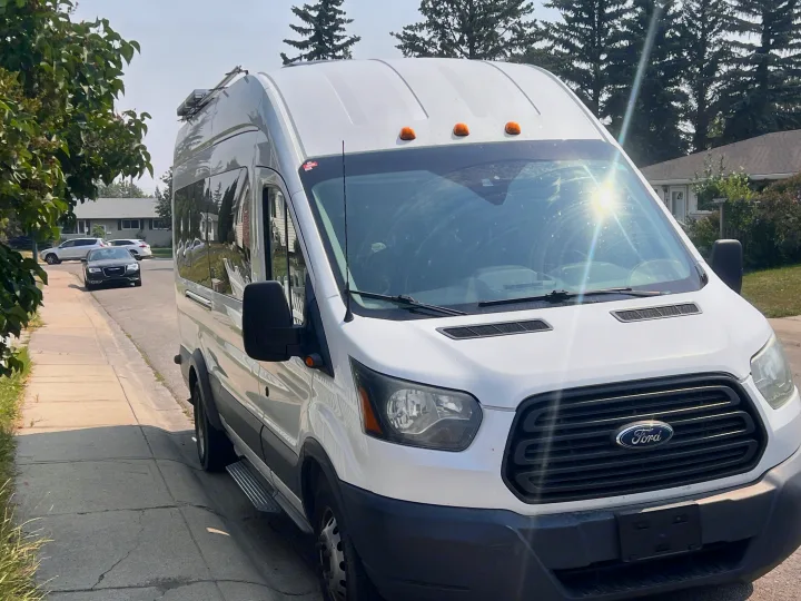 Front view of a white Ford Transit camper van, likely an rv rental, parked on a sunny residential street.. Ford Transit 2016