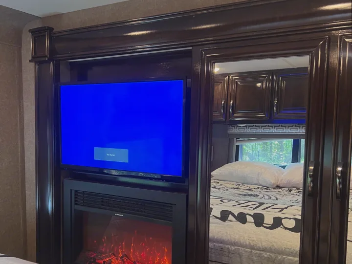 RV rental bedroom with a wall-mounted TV, electric fireplace, and mirrored cabinet doors reflecting the patterned bed.. Thor Quantum 2017