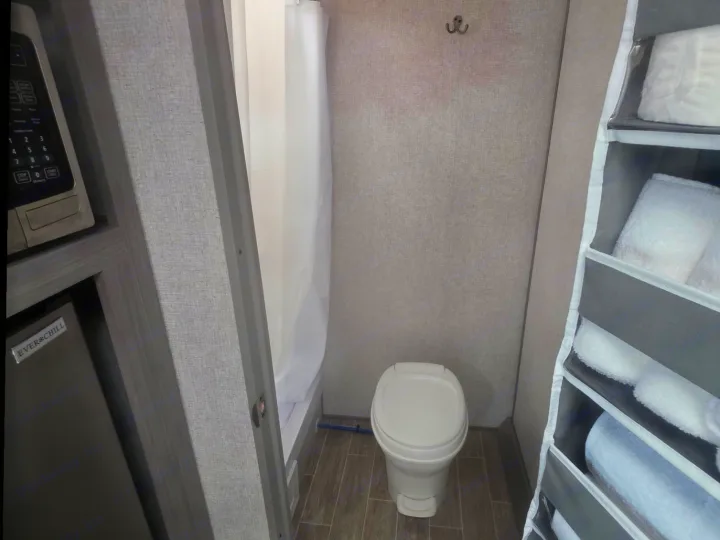 Compact RV rental bathroom with toilet, shower, towel storage, microwave, and mini-fridge.. Dutchmen Coleman Lantern LT 2022