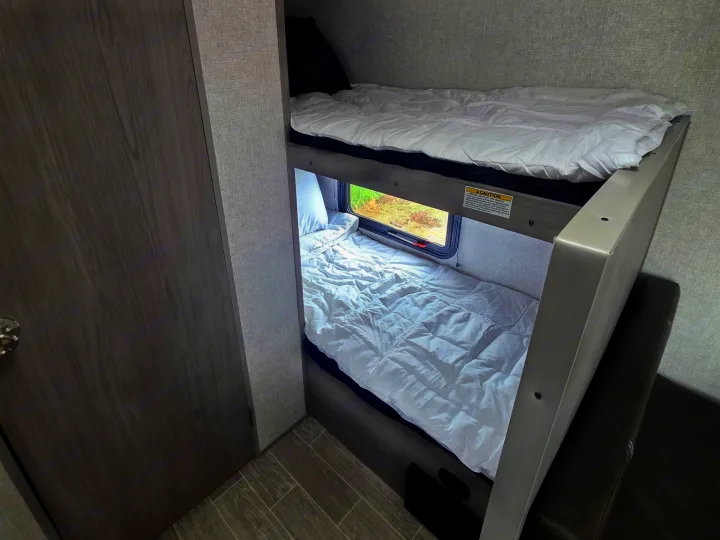 RV rental bunk beds provide cozy sleeping space inside a modern camper, with a window by the lower bunk.. Dutchmen Coleman Lantern LT 2022