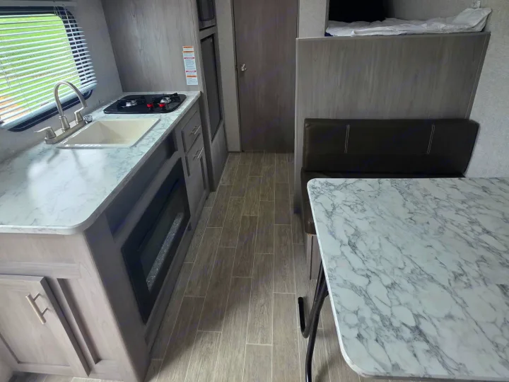 RV rental interior: kitchen with sink, stovetop, & electric fireplace, plus a dinette and bunk bed. Clean, compact design.. Dutchmen Coleman Lantern LT 2022