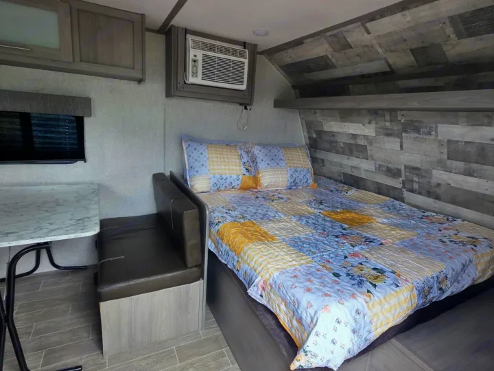 RV rental interior featuring a cozy bedroom with a patchwork quilt, AC, and small dinette.. Dutchmen Coleman Lantern LT 2022