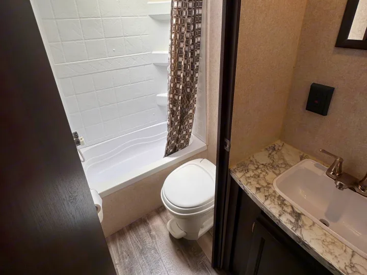 Compact RV rental bathroom with a bathtub/shower, toilet, and sink vanity with a marble-look countertop.. Jayco Jay Flight SLX 2020