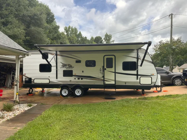 A white Jayco Jay Flight SLX travel trailer RV rental with its awning extended is parked on a concrete driveway.. Jayco Jay Flight SLX 2020