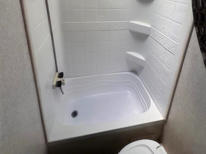 Bright, clean RV rental bathroom featuring a white shower/tub combo, corner shelves, and a flexible showerhead. Toilet visible.. Jayco Jay Flight SLX 2020