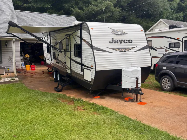 A Jayco travel trailer is parked on a driveway with an extended awning. This RV rental is stabilized and ready for adventure.. Jayco Jay Flight SLX 2020