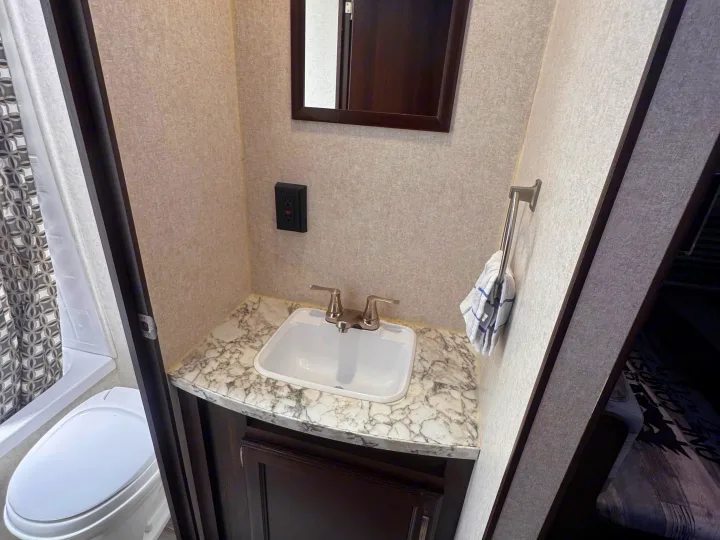 RV rental bathroom with a sink, mirror, GFI outlet, toilet, and shower curtain. Compact and functional for travel.. Jayco Jay Flight SLX 2020