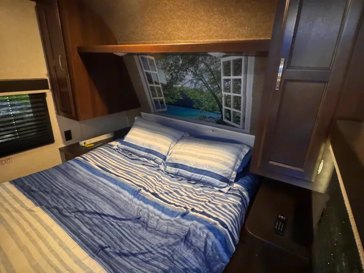 Cozy RV rental bedroom featuring blue striped bedding, a scenic window mural above the bed, and dark wood cabinets.. Jayco Jay Flight SLX 2020