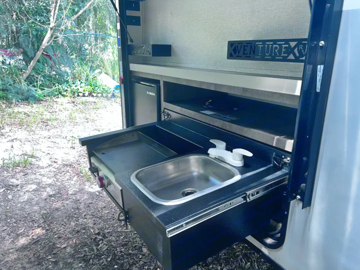 This RV rental's outdoor kitchen features a pull-out sink, griddle, and mini-fridge, ideal for camp cooking amidst nature.. Sonic Sonic Trailer 2022