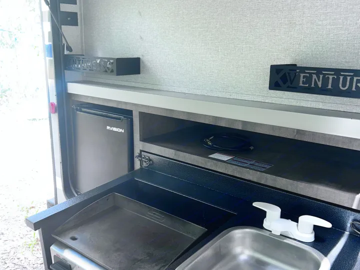 This rv rental features an outdoor kitchen with an RVISION fridge, Coleman griddle, and sink, perfect for campsite cooking.. Sonic Sonic Trailer 2022