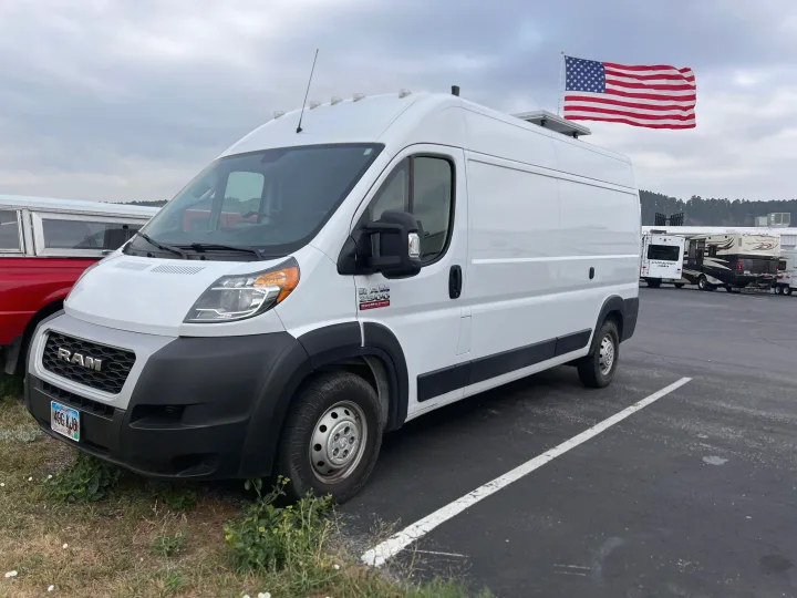 White Ram ProMaster camper van, with an American flag mounted on the roof, parked near other RVs. Great for rv rental.. Dodge Ram Promaster 2500 2020