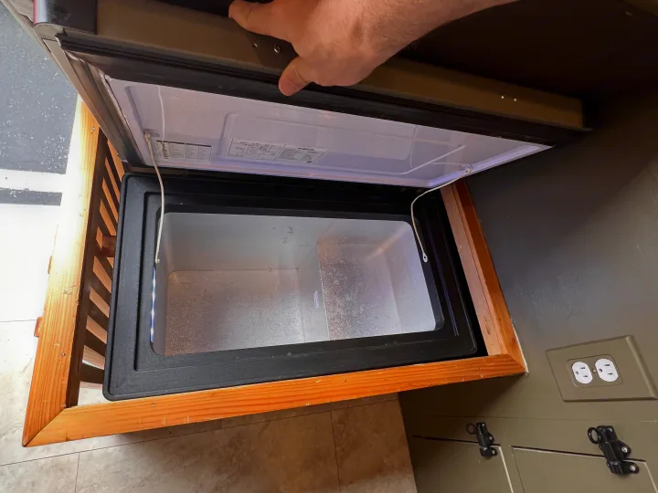 Accessing the compact, built-in freezer/fridge in an **RV rental** kitchen. The top lid is open, revealing the empty interior.. Dodge Ram Promaster 2500 2020
