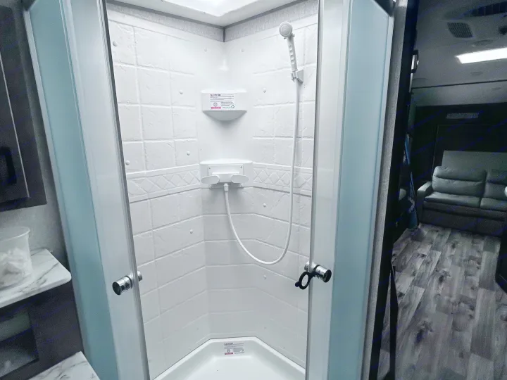 Inside an RV rental, this clean shower stall has frosted doors, a handheld shower, and a shelf. A dark sofa is visible outside.. Sonic Sonic Trailer 2022