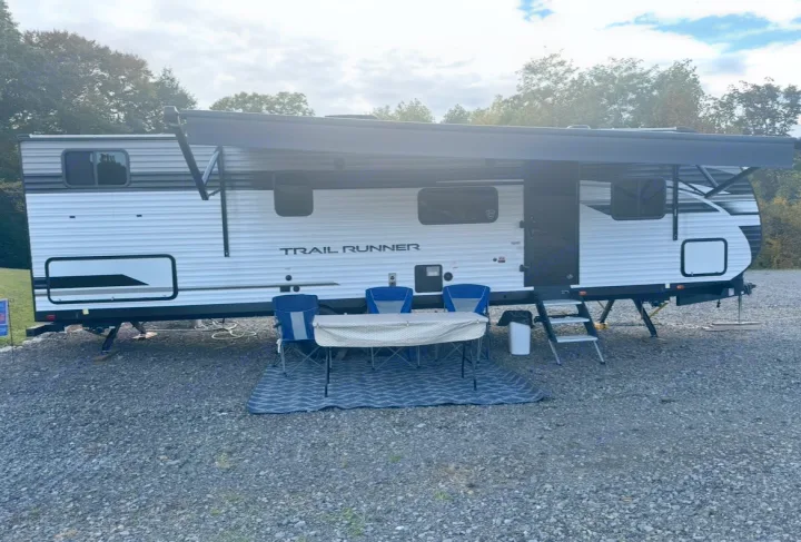 RV rental: A white and black Trail Runner travel trailer with awning extended at a gravel campsite, table and chairs set up.. Forest River Cherokee 2022