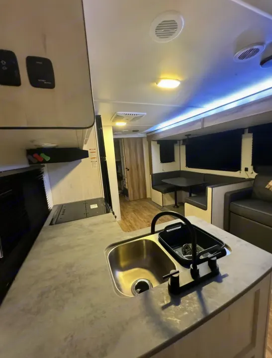 Well-lit modern RV rental interior showing a kitchen with sink, dinette, and lounge area. Ready for your travels.. Forest River Cherokee 2022