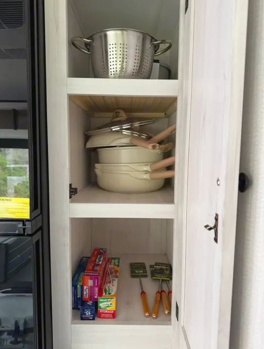 RV rental kitchen cabinet showing neatly stored pots, pans, colander, and food storage bags for efficient cooking.. Forest River Cherokee 2022