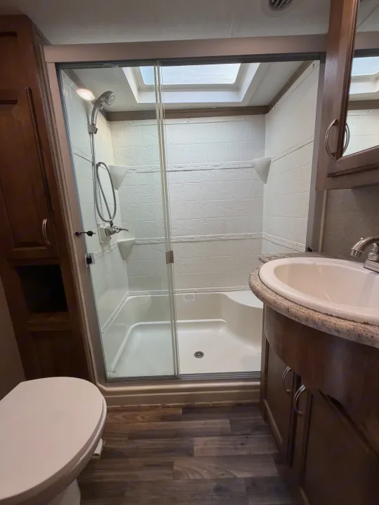 RV rental bathroom features a well-lit shower with skylight & glass door, sink, and toilet for comfortable travel.. Forest River Coachmen Chaparral 2015