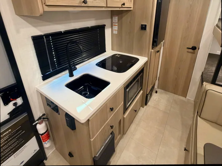 RV rental interior: A well-equipped camper kitchen featuring a sink, stovetop, microwave, and stylish cabinetry.. Forest River Rockwood Geo Pro 17LE 2026