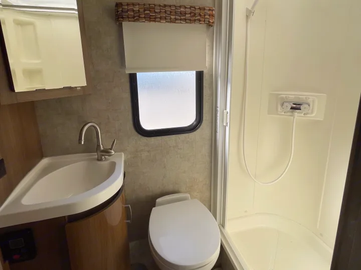 Compact RV rental bathroom featuring a corner sink, toilet, and shower stall, designed for efficient space use.. Winnebago Trend 2015