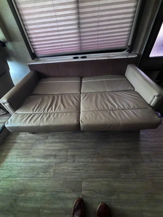 Relax in this rv rental! View of a comfortable gray sofa bed extended, with window blinds, cup holders, and laminate flooring.. Thor Resonate 2024
