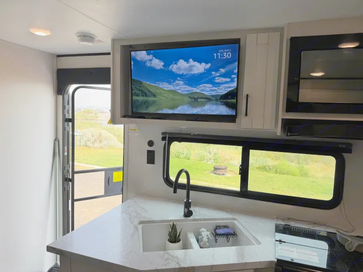 RV rental kitchen with marble counter, sink, TV showing a lake, and open door to a green outdoor landscape.. Jayco Jay-flight 2026
