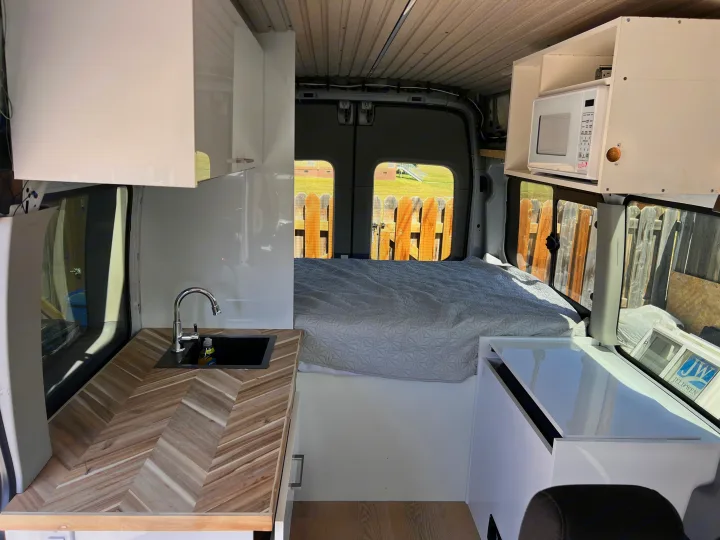 Step into this modern van conversion, featuring a compact kitchenette, comfortable bed, and microwave – ideal for an rv rental.. Ford Transit 2016