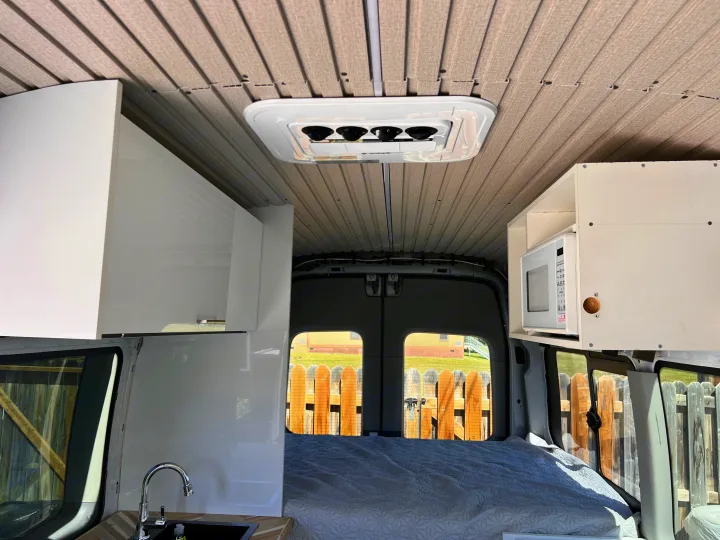 RV rental interior with overhead AC, microwave, sink, and bed, showing a cozy van conversion.. Ford Transit 2016
