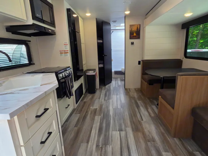 Bright rv rental interior featuring a modern kitchen, dinette, and wood floors. Fridge, microwave, and bathroom visible.. Jayco Jay Flight SLX 2026
