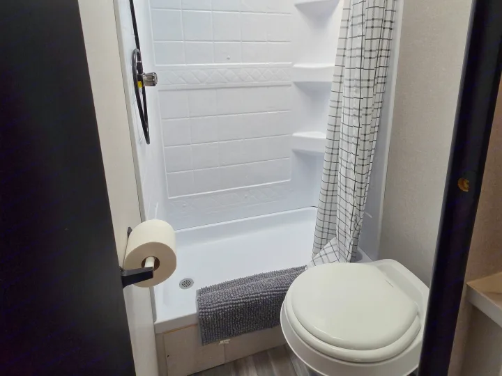 Compact RV rental bathroom with shower, toilet, and checkered curtain, showing efficient use of space.. Jayco Jay Flight SLX 2026