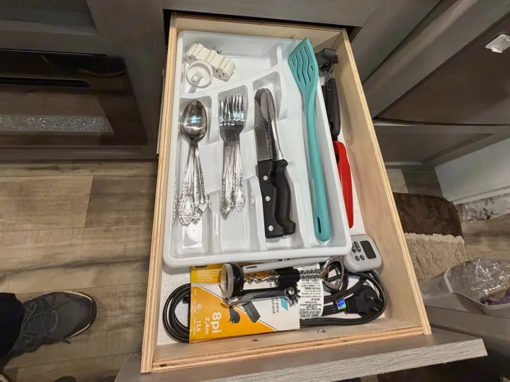 Inside an RV rental kitchen drawer: organized cutlery, spatula, can opener, multi-outlet adapter, and extension cord.. Dutchmen Coleman 2024