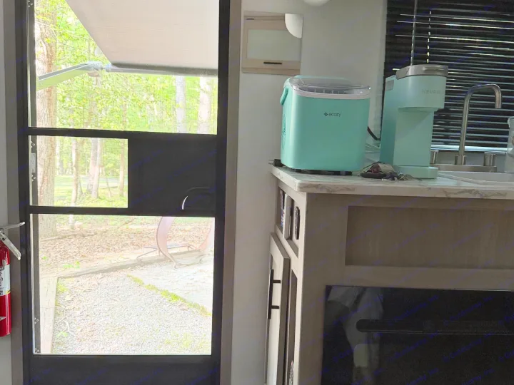 Inside an RV rental: screen door views nature, with an Ecozy ice maker, Keurig coffee machine, sink, and fire extinguisher.. Dutchmen Coleman 2024